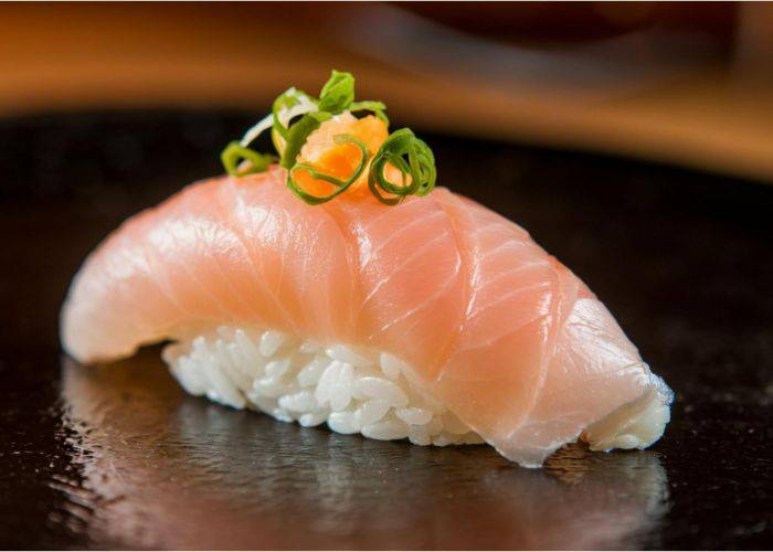 Kaburazushi (fermented yellowtail sushi), resting on a black serving plate and garnished with spring onions.