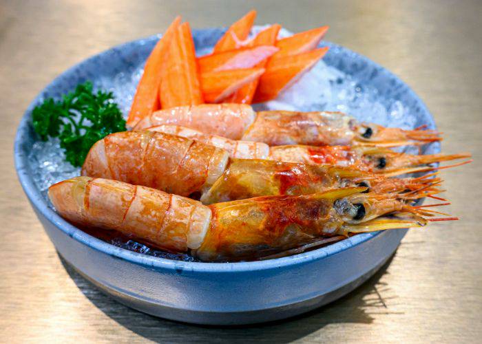 Amaebi (sweet shrimp) in a blue bowl, served on ice alongside herbs and vegetables.