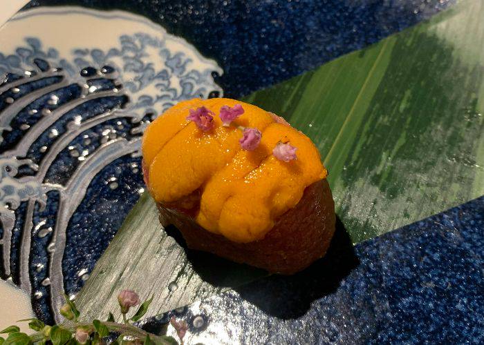 The wagyu-wrapped sea urchin nigiri sushi, garnished with pink flowers from the shiso plant.