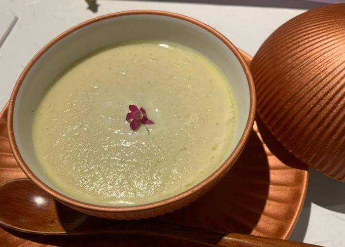 A creamy yellow dish in a vibrant copper pot: chawanmushi. A single flower adorns it.