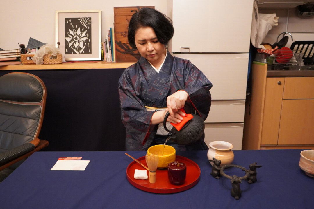 A host pouring Japanese tea while wearing a kimono.