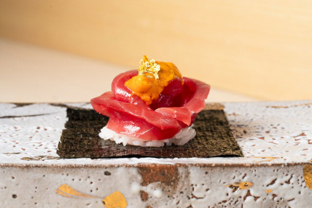 Tuna sushi in the shape of a flower topped with uni and edible gold leaves