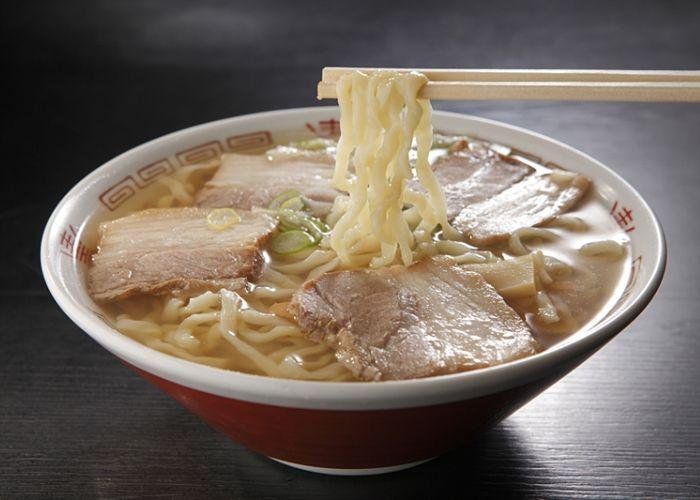 A steaming bowl of Kitakata ramen with chopsticks holding the noodles and slices of pork on top