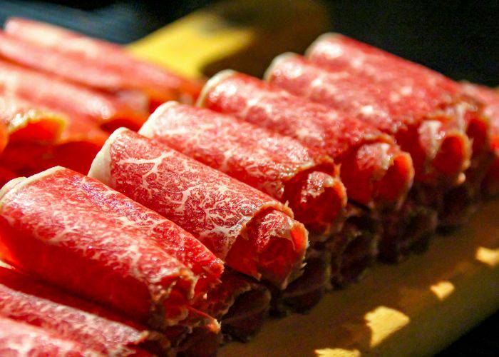 Thin, rolled slices of wagyu beef, likely waiting to be dunked in a Japanese hot pot.