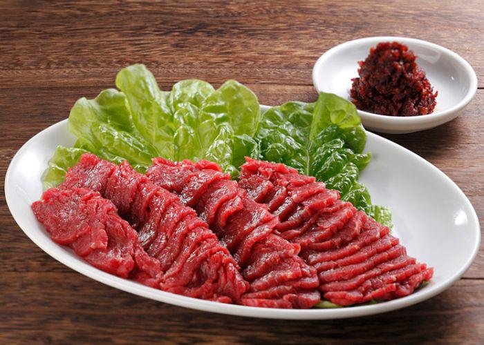 A plate of raw horsemeat with lettuce on the side and a dish of hot soybean paste on the side