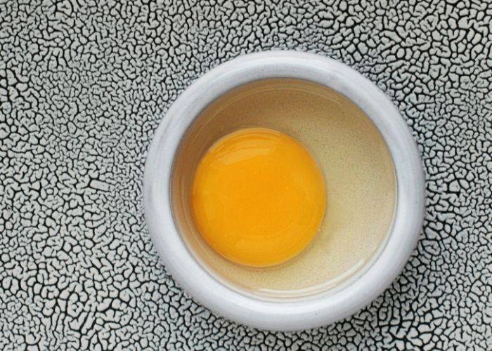 A raw egg in a white bowl with a textured background.