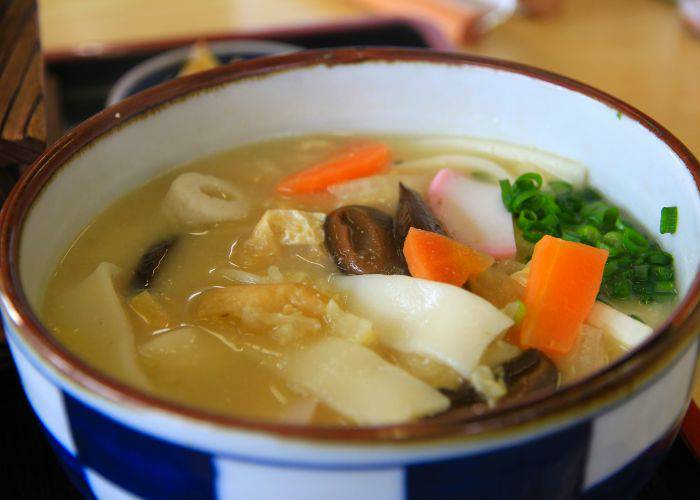 A fresh bowl of dango-jiru, featuring long noodles, carrots, fish cake, mushrooms and spring onion in a miso-based broth.