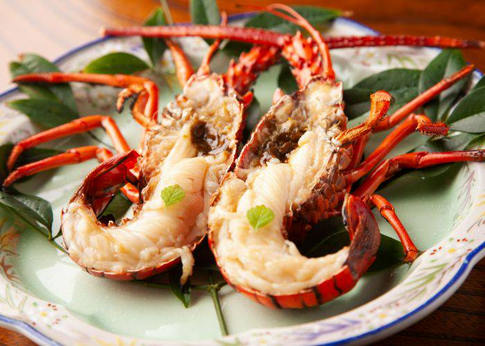 A cooked spiny lobster, split in half and garnished with herbs.