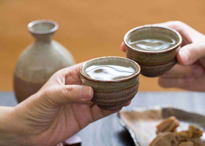 Two full cups of sake being clinked in cheers.