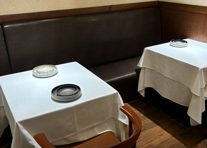 The minimal interiors of HOMMAGE. Tables are set with white tablecloths and prepared with stacked dishes.