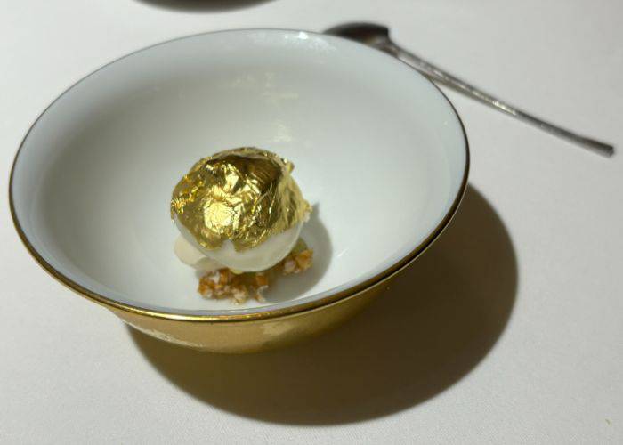 Soft soy milk-based blancmange mousse filled with sorbet on a bed of crispy sweet peanut and rice crackers, elegantly topped with a gold leaf.