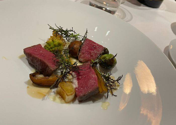 A stylish plating of wagyu beef at Osteria Bacco, garnished with herbs.