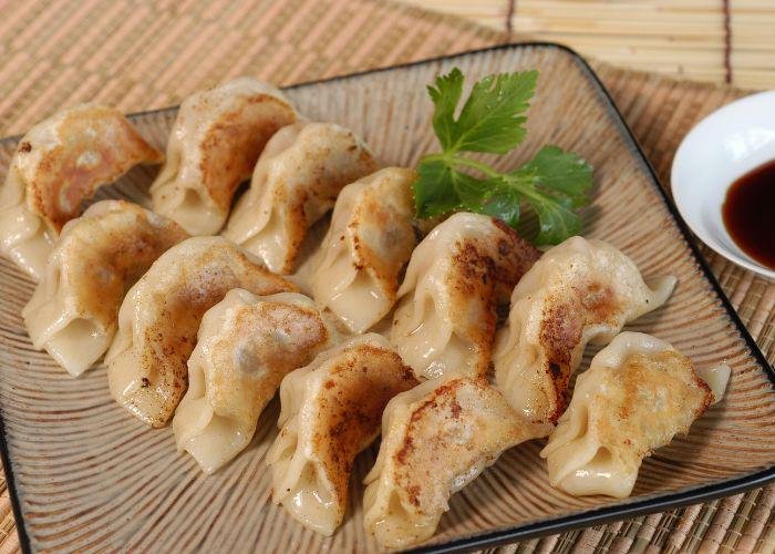 A plate with a dozen pan fried gyozas with a side of soy sauce  