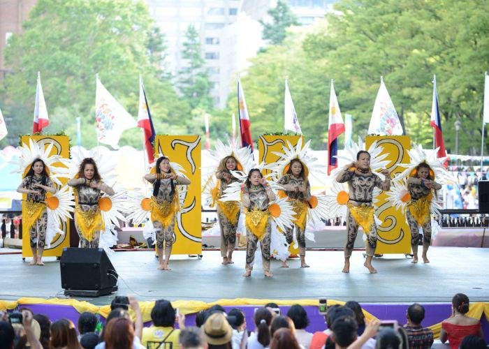 A group of performers on stage at the Philippines festival dressed in costumes with big white daisy's on