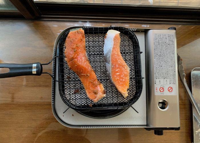 Two bright orange salmon fillets are grilling over a portable burner