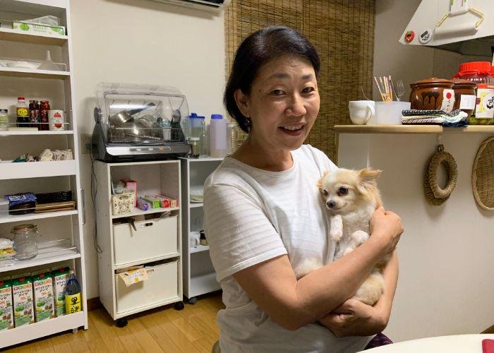 A dark-haired owman bugging her small chihuahua, Colin, in her Japanese kitchen