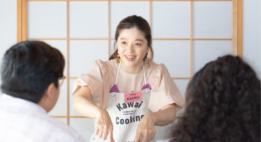 A smiling instructor helping two guests with cooking.