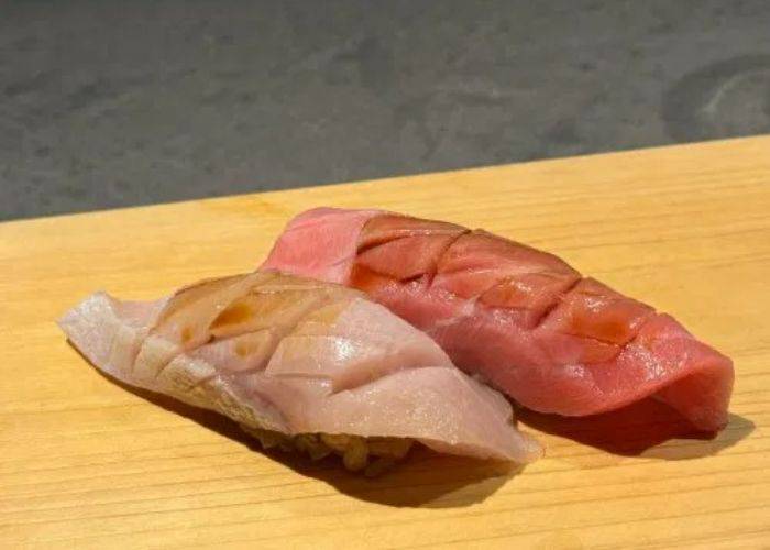 Two pieces of nigiri sushi; the fish is crosshatched for soaking up soy sauce.