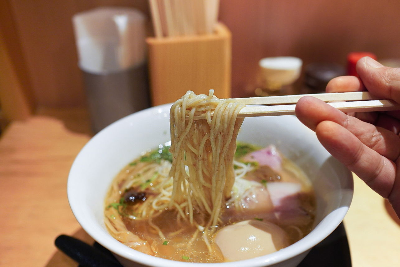 Someone picking up noodles from a rich, porcini ramen broth at Sobahouse Konjikihototogisu.