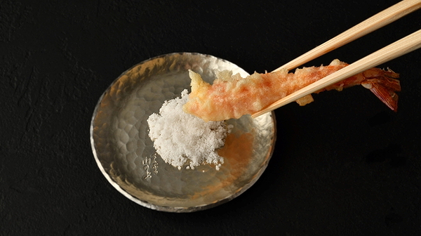 Chopsticks holding tempura shrimp with dipping salt