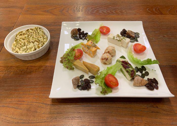 A plate of vegan cheeses that are made in-house, garnished with slices of tomato and lettuce