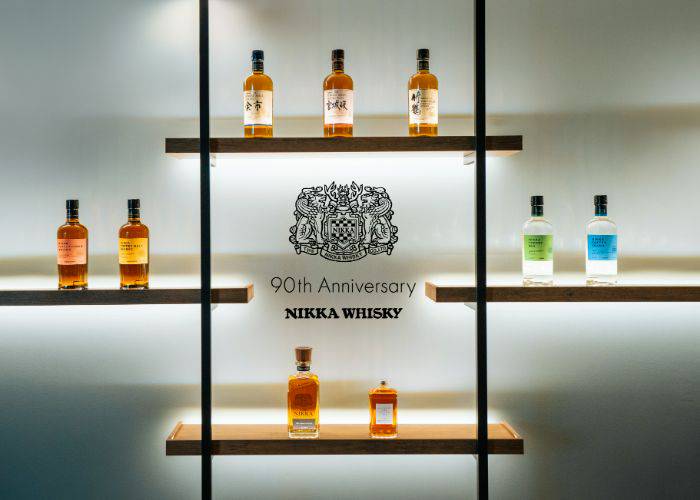 Four shelves featuring bottles of NIKKA WHISKY; at its center, 90th Anniversary NIKKA WHISKY is written.