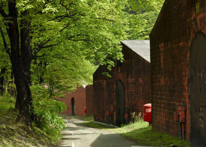 The exterior of one of NIKKA WHISKY distilleries, showing traditional red brick against the green of nature.