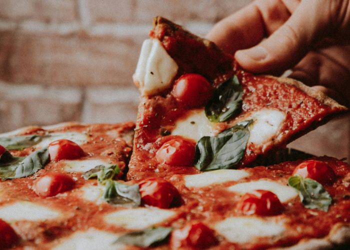 Someone taking a slice of a margherita pizza, topped with mozzarella, basil and tomato.