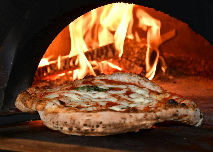 A pizza being delivered into a woodfired pizza oven.