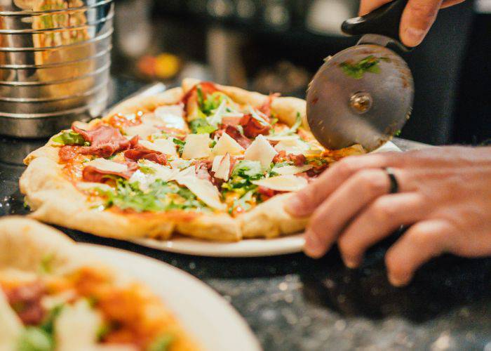 Someone slicing a pizza with a round pizza cutter.