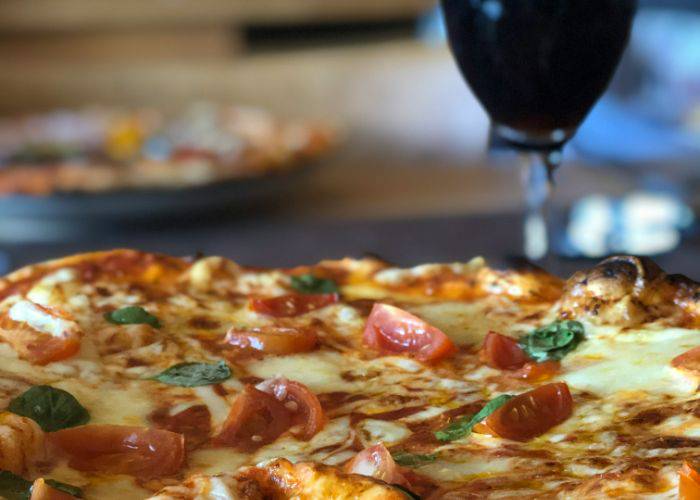 A cheesy margherita pizza with a drink in the background.