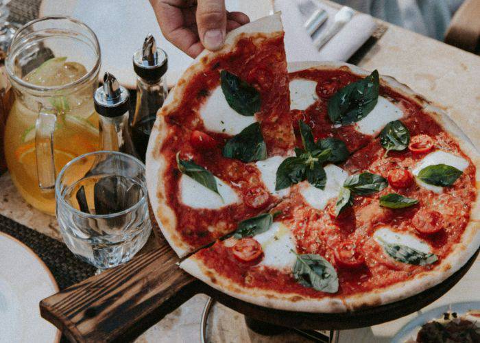 Someone picking up a slice of pizza from a wooden board.