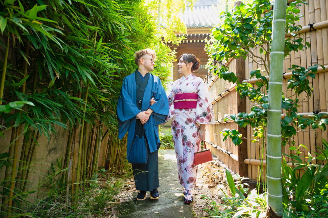 A newly-wed couple walking along a path bordered by vivid green bamboo.