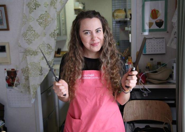 A girl, Birim, who is wearing a pink apron holds two sharp knives and smiles 