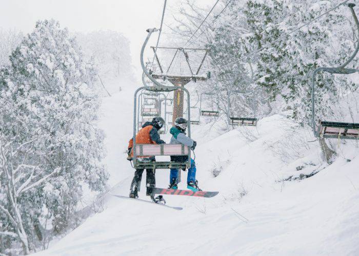 Two snowboarders riding the chairlift in Hakuba, perfect for winter sports.