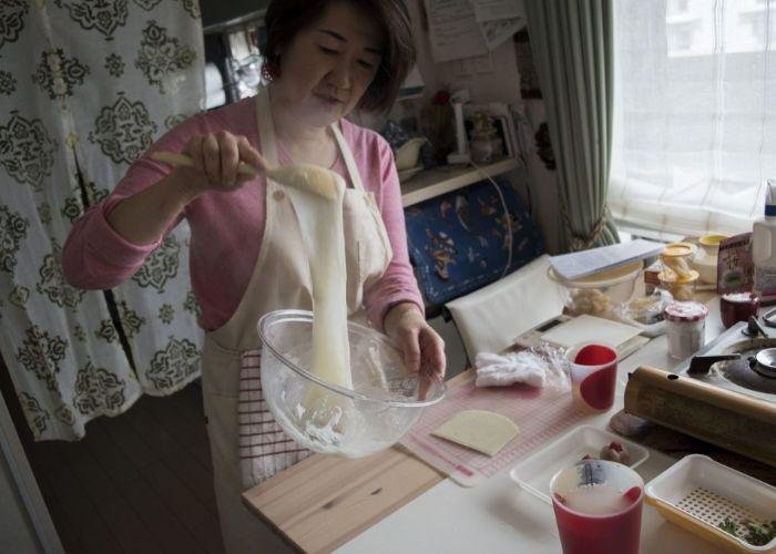 Miyuki-san, the teacher of the mochi and wagashi making class, shows how to make mochi. She is wearing an apron and stirs a sticky ball of mochi