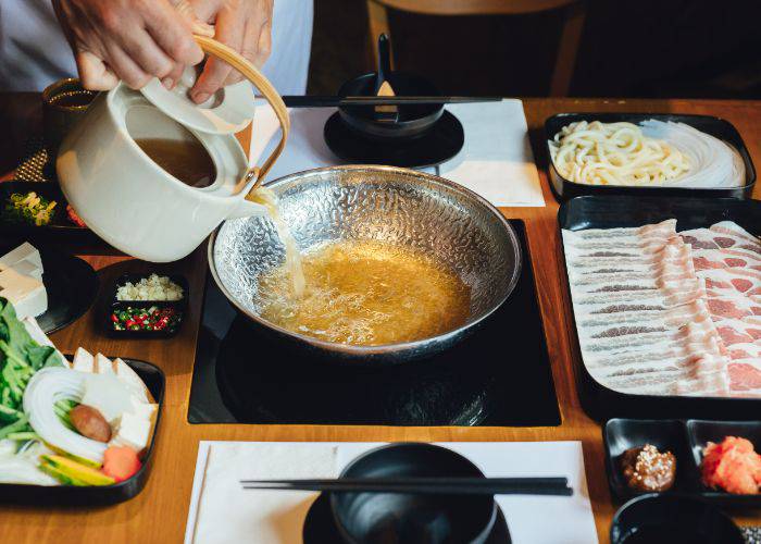 Someone pouring a flavorful broth into a central bowl for Japanese hot pot.