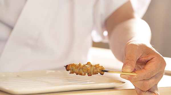 Chef holding a grilled skewer on a minimalist plate