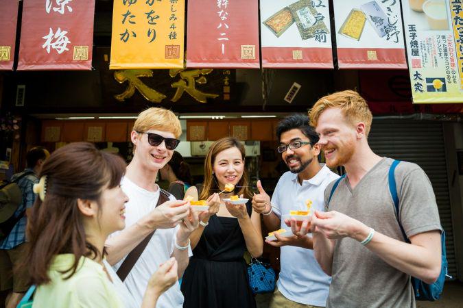 A food tour group discussing in front of a market while tasting food sample  