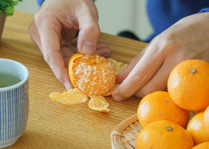 Someone peeling Japanese mikan on a table, next to a fresh cup of green tea.