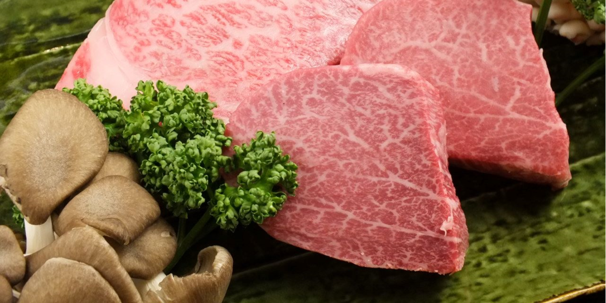 Premium Wagyu beef slices with fresh herbs and mushrooms on a green plate