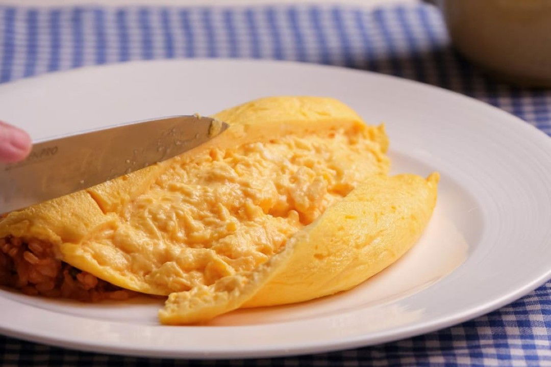 An omurice omelet being sliced open with a knife.