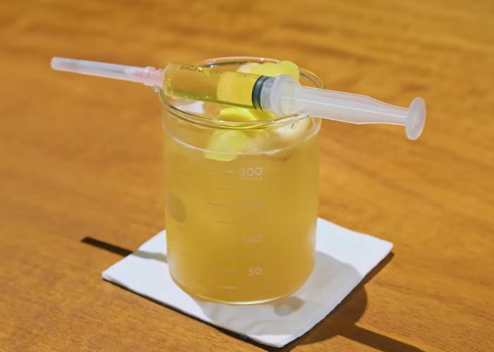 A whiskey-based cocktail with a syringe of peated whiskey resting on top at APOTHECA in Kyoto.