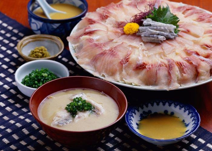 A plate of thinly sliced kankoi (koi, or carp) sashimi is laid out on a table along with miso soup, dipping sauce, chives, and other small dishes
