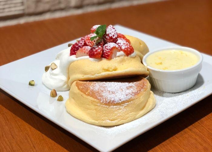 Fluffy Japanese pancakes on a square plate with a dollop of whipped cream and chopped nuts