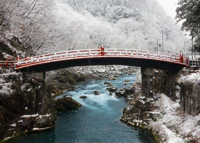 Nikko's iconic Shinkyo Bridge, seen in winter; a light dusting of snows frames the scene.