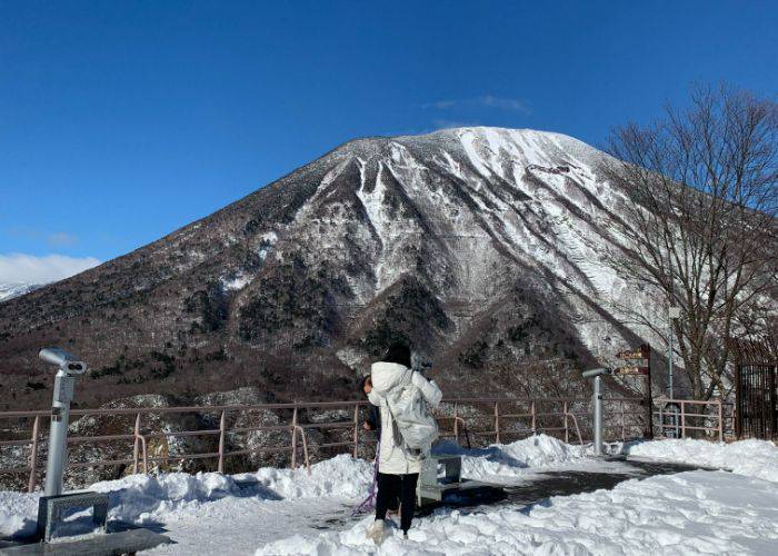 The author of this blog wearing a thick coat, looking out at snowy mountains in Nikko.