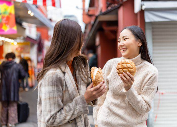 Two girls smiling in Asakusa while holding cream-filled melon pan.