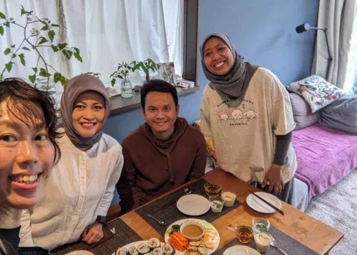 Smiling guests in a home-cooking class in Tokyo; the table is filled with Japanese food.