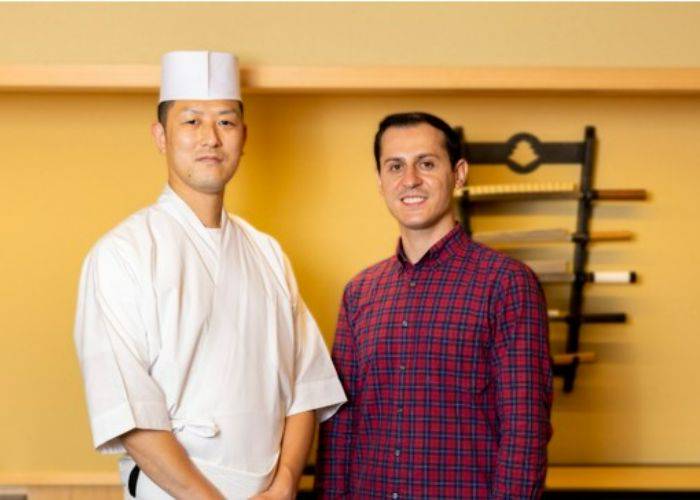 Serkan smiling at the camera, standing beside a chef in Japan.